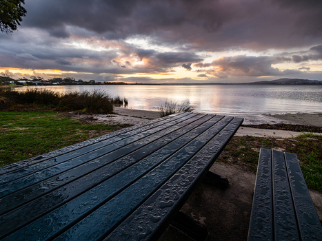 View of a wet wooden picnic table overlooking the calm waters of Oyster Harbour at sunset in Little Grove Western Australia Australia. View of a wet wooden picnic table overlooking the calm waters of Oyster Harbour at sunset in Little Grove Western Australia Australia.
