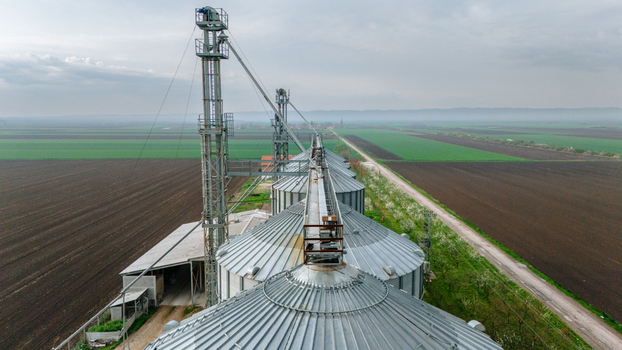 Aerial view of metallic silos standing tall against the backdrop of agricultural fields where dark earth meets vibrant greenery Sremska Mitrovica Vojvodina Serbia. Aerial view of metallic silos standing tall against the backdrop of agricultural fields where dark earth meets vibrant greenery Sremska Mitrovica Vojvodina Serbia.