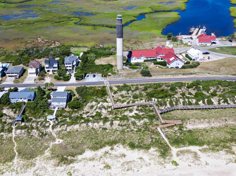 Aerial view of Oak Island Lighthouse surrounded by coastal dunes wooden boardwalks and residential houses near the Atlantic Ocean in Caswell Beach North Carolina United States.