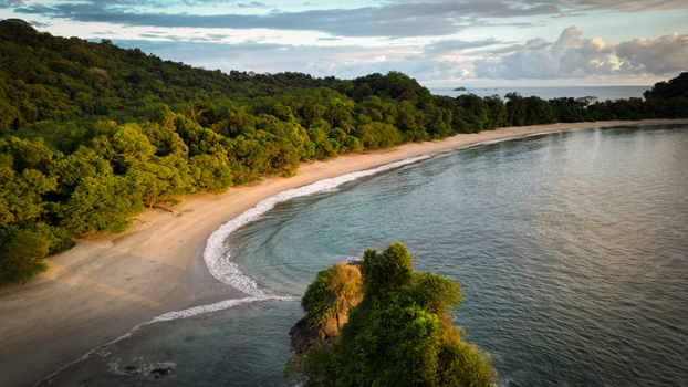 Aerial view of a pristine beach curving gently into the turquoise sea fringed by a dense emerald rainforest Quepos Puntarenas Province Costa Rica.