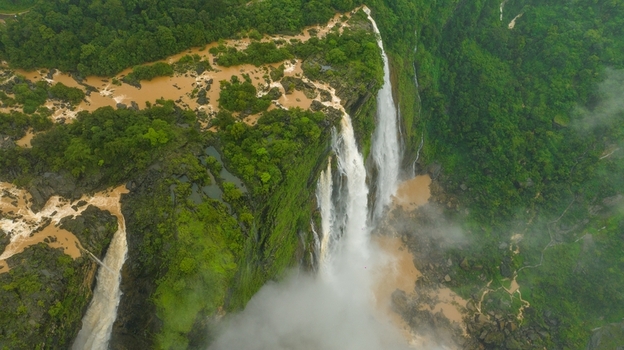 Aerial view of Jog Falls cascading down lush green cliffs into a misty pool surrounded by dense tropical forest in Kargal Karnataka India.