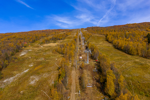 Aerial view of a ski slope in autumn with chairlift infrastructure and vibrant yellow trees under a clear blue sky in Bjorli Innlandet Norway. Aerial view of a ski slope in autumn with chairlift infrastructure and vibrant yellow trees under a clear blue sky in Bjorli Innlandet Norway.