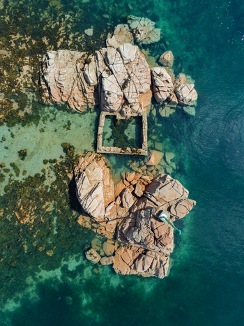 Aerial view of the rocky coastline and a stone tidal pool surrounded by clear turquoise water near the island of Ile de Brehat Brittany France.