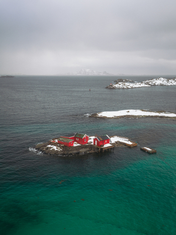Aerial view of red houses on a snow dusted island embraced by the turquoise sea under a cloudy sky Svolv&aelig;r Nordland Norway.