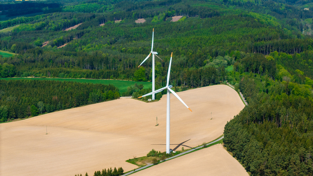 Aerial view of the Zipotin wind turbines standing in golden fields surrounded by dense green forests and rolling hills in Gruna Pardubicky kraj Czechia. Aerial view of the Zipotin wind turbines standing in golden fields surrounded by dense green forests and rolling hills in Gruna Pardubicky kraj Czechia.