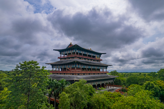 Aerial view of a traditional multi story pagoda temple surrounded by lush green forest under a dramatic cloudy sky in Nepal.