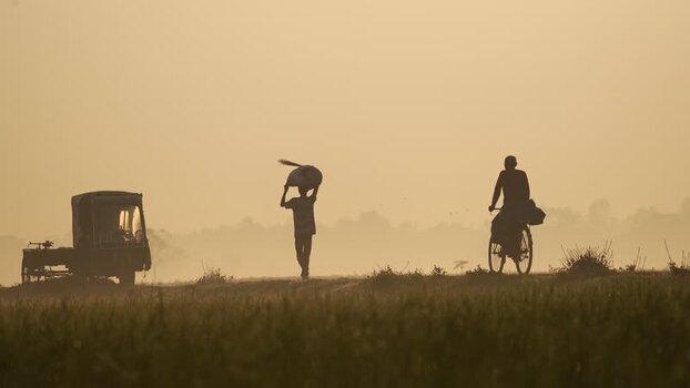 View of silhouettes of workers and a cyclist in a misty field Bangladesh. View of silhouettes of workers and a cyclist in a misty field Bangladesh.