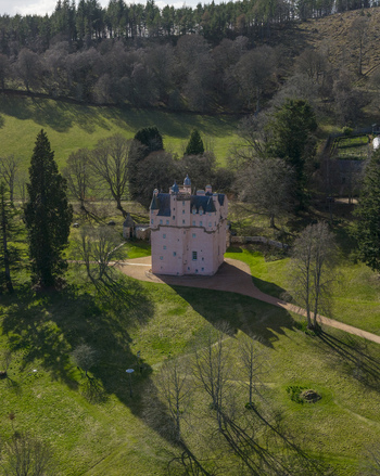 Aerial view of the iconic pink Craigievar Castle surrounded by lush green lawns and dense woodland in Craigievar Scotland United Kingdom.