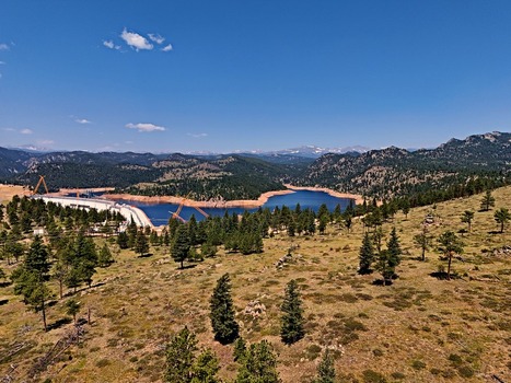 Aerial view of Walker Ranch reservoir and dam surrounded by pine forests and rolling hills under a clear blue sky in Boulder Colorado United States.