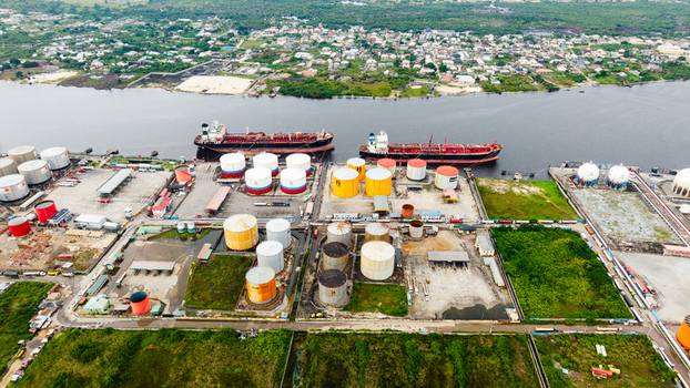 Aerial view of the industrial oil storage facility in Satellite Town featuring storage tanks pipelines and cargo ships docked along the riverbank in Lagos Lagos Nigeria.
