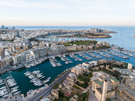 Aerial view of a bustling marina filled with white yachts and sailboats surrounded by dense urban architecture and modern apartment buildings in Malta. Aerial view of a bustling marina filled with white yachts and sailboats surrounded by dense urban architecture and modern apartment buildings in Malta.
