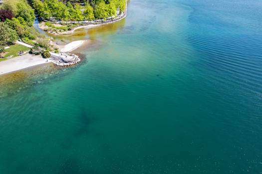 Aerial view of the turquoise waters of Lake Geneva along the lush green shoreline with people relaxing on the beach in Morges Vaud Switzerland. Aerial view of the turquoise waters of Lake Geneva along the lush green shoreline with people relaxing on the beach in Morges Vaud Switzerland.