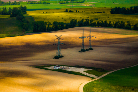 Aerial view of rolling agricultural fields with power pylons and a small utility building under golden hour light in Brno South Moravian Region Czechia.