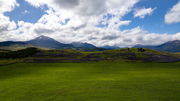 Aerial view of lush green fields and rolling hills set against the backdrop of the Andes mountains under a bright blue sky in Coyhaique Aysen Chile. Aerial view of lush green fields and rolling hills set against the backdrop of the Andes mountains under a bright blue sky in Coyhaique Aysen Chile.