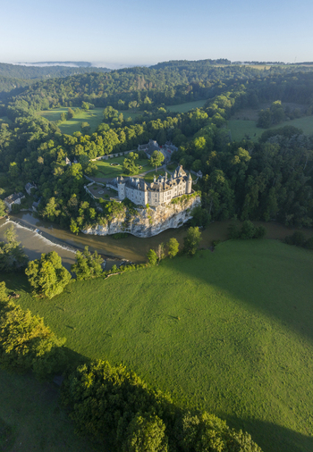 Aerial view of the historic Chateau de Walzin perched on a rocky cliff above the Lesse river surrounded by lush green forests and meadows in Dinant Region wallonne Belgium.