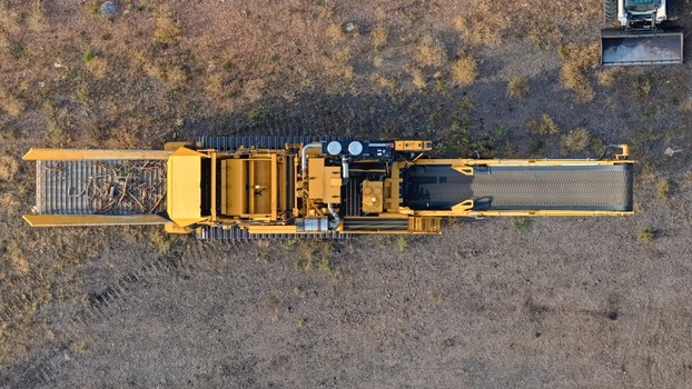 Aerial view of a yellow industrial mobile crusher machine with a long conveyor belt and tracks positioned on a gravel site in Golden Colorado United States.