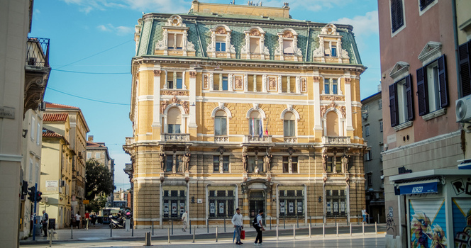 Rijeka Croatia 19 September 2026 View of a historic building with ornate yellow facade and green roof featuring detailed architectural carvings situated along a pedestrian street with people. Rijeka Croatia 19 September 2026 View of a historic building with ornate yellow facade and green roof featuring detailed architectural carvings situated along a pedestrian street with people.
