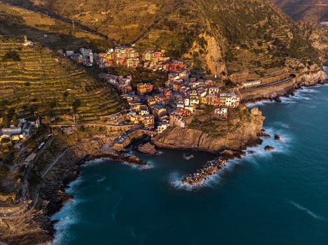 Aerial view of the colorful houses of Manarola village perched on rugged cliffs with terraced hillsides and the blue Mediterranean sea at sunset Manarola Liguria Italy.