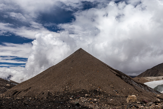 View of the pyramid shaped moraine of Baltoro Glacier with rocky terrain under a dramatic cloudy sky in Baltoro Gilgit Baltistan Pakistan.