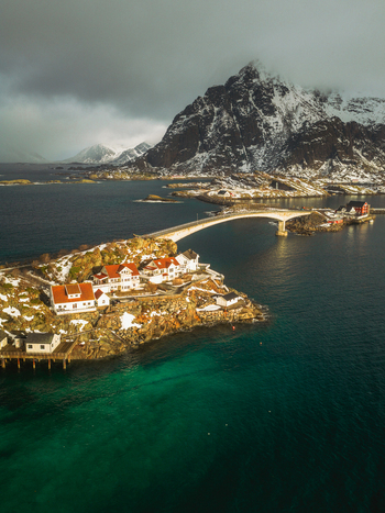 Aerial view of the village connected by bridges with snow capped mountains looming in the background Henningsv&aelig;r Nordland Norway.