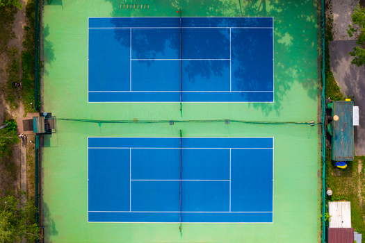 Aerial view of two blue tennis courts set on a green surface surrounded by trees in Warsaw Masovian Voivodeship Poland. Aerial view of two blue tennis courts set on a green surface surrounded by trees in Warsaw Masovian Voivodeship Poland.