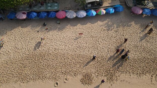 Aerial view of Indrayanti Beach with colorful umbrellas lining the sandy shore and people walking on the beach in Kecamatan Tepus Daerah Istimewa Yogya Indonesia. Aerial view of Indrayanti Beach with colorful umbrellas lining the sandy shore and people walking on the beach in Kecamatan Tepus Daerah Istimewa Yogya Indonesia.