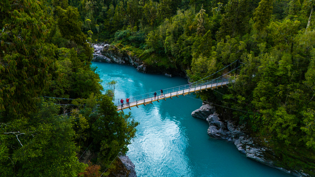 Aerial view of the vivid turquoise river snaking through the Hokitika Gorge where a suspension bridge stretches between verdant cliffs Kokatahi West Coast Region New Zealand. Aerial view of the vivid turquoise river snaking through the Hokitika Gorge where a suspension bridge stretches between verdant cliffs Kokatahi West Coast Region New Zealand.