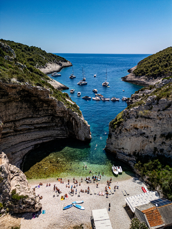 Aerial view of Stiniva beach with its iconic narrow cliff opening turquoise waters anchored boats and people on the pebble shore in Vis Split Dalmatia County Croatia.