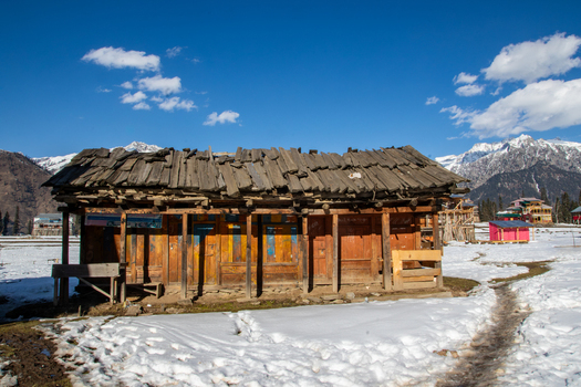 View of a traditional wooden house with a weathered roof set against a backdrop of snow covered mountains in Arang Kel Kashmir Pakistan. View of a traditional wooden house with a weathered roof set against a backdrop of snow covered mountains in Arang Kel Kashmir Pakistan.