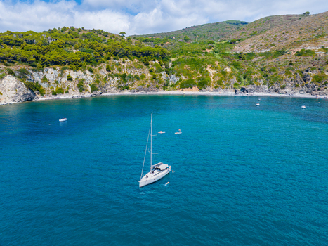 Aerial view of a white sailboat anchored in the turquoise waters of a bay near the rocky coastline of Capoliveri Tuscany Italy.