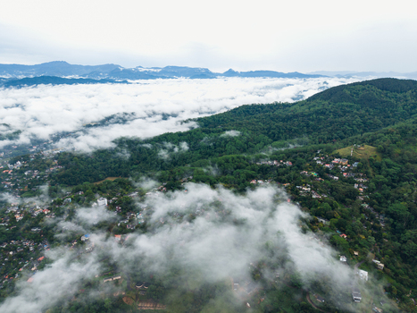 Aerial view of lush green hills and urban settlements partially covered by thick white mist under an overcast sky in Kandy Central Province Sri Lanka. Aerial view of lush green hills and urban settlements partially covered by thick white mist under an overcast sky in Kandy Central Province Sri Lanka.