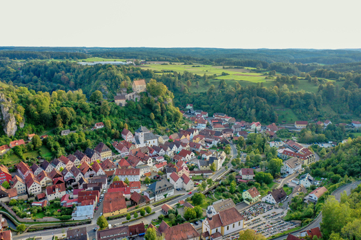 Aerial view of Pottenstein Castle overlooking the historic town with red roofed houses and lush green hills in Pottenstein Bavaria Germany. Aerial view of Pottenstein Castle overlooking the historic town with red roofed houses and lush green hills in Pottenstein Bavaria Germany.