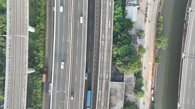 Aerial view of a multi lane highway with moving vehicles and parallel railway tracks alongside a river and lush greenery in Bekasi Barat West Java Indonesia. Aerial view of a multi lane highway with moving vehicles and parallel railway tracks alongside a river and lush greenery in Bekasi Barat West Java Indonesia.