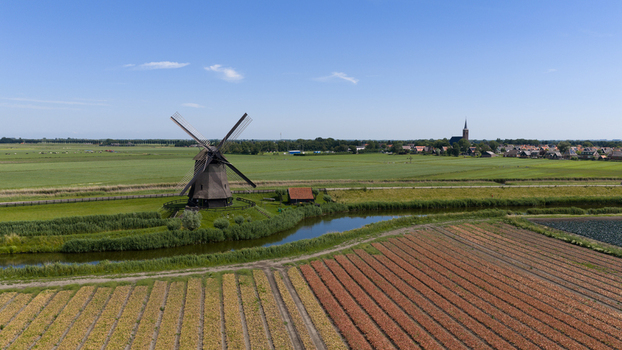 Aerial view of Bovenmolen G windmill surrounded by lush green fields a winding canal and agricultural rows under a clear blue sky in Schermerhorn Noord Holland Netherlands. Aerial view of Bovenmolen G windmill surrounded by lush green fields a winding canal and agricultural rows under a clear blue sky in Schermerhorn Noord Holland Netherlands.
