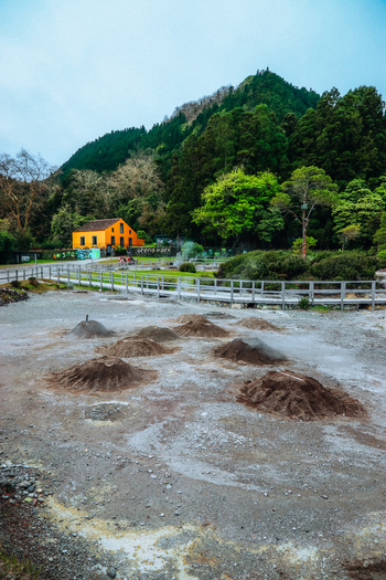View of a vibrant yellow house nestled against a backdrop of lush green trees overlooking geothermal ground a scene of natural wonder Furnas Azores Portugal.