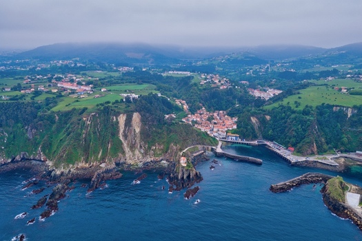 Aerial view of the historic fishing village of Cudillero nestled between steep green cliffs and the blue waters of the Cantabrian Sea under a misty sky Cudillero Asturias Spain. Aerial view of the historic fishing village of Cudillero nestled between steep green cliffs and the blue waters of the Cantabrian Sea under a misty sky Cudillero Asturias Spain.