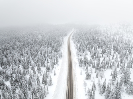 Aerial view of a road winding through a dense snow covered forest near Yllas in Kolari Lapland Finland.
