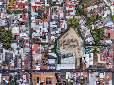 Aerial view of the urban landscape featuring dense residential rooftops narrow streets and a central construction site with heavy machinery surrounded by greenery. Uruapan Michoacan Mexico. Aerial view of the urban landscape featuring dense residential rooftops narrow streets and a central construction site with heavy machinery surrounded by greenery. Uruapan Michoacan Mexico.