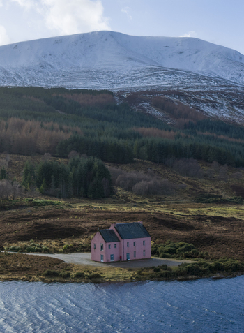 Aerial view of The Pink House on the shore of Loch Glass with a snow capped mountain and dense pine forest in the background Dingwall Scotland United Kingdom. Aerial view of The Pink House on the shore of Loch Glass with a snow capped mountain and dense pine forest in the background Dingwall Scotland United Kingdom.
