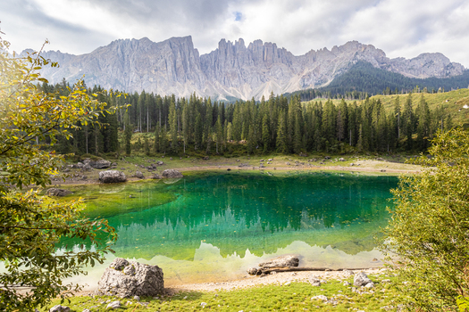 View of Karersee with vibrant emerald green water reflecting the dense coniferous forest and jagged Latemar mountain peaks in Welschnofen Trentino Alto Adige Italy.