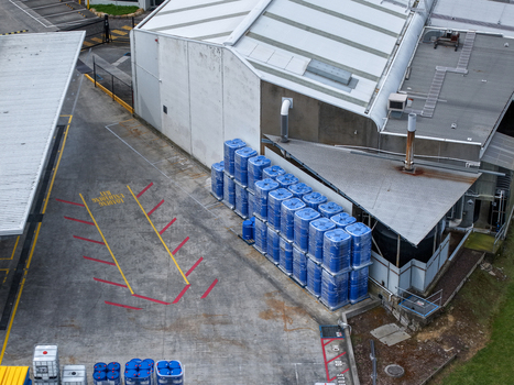 Melbourne VIC Australia 25 September 2026 Aerial view of an industrial site with stacked blue plastic containers concrete loading area with markings and metal warehouse buildings.