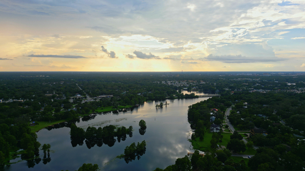 Aerial view of a residential neighborhood featuring a calm lake surrounded by lush trees and houses under a dramatic sunset sky in Tampa Florida United States. Aerial view of a residential neighborhood featuring a calm lake surrounded by lush trees and houses under a dramatic sunset sky in Tampa Florida United States.