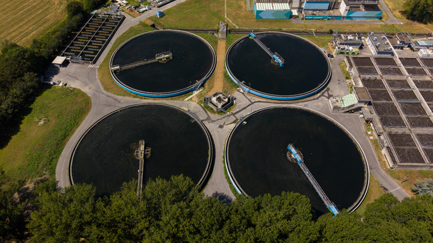 Aerial view of a wastewater treatment plant featuring four large circular sedimentation tanks with mechanical arms surrounded by industrial infrastructure and green trees in Milan Lombardy Italy. Aerial view of a wastewater treatment plant featuring four large circular sedimentation tanks with mechanical arms surrounded by industrial infrastructure and green trees in Milan Lombardy Italy.