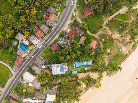 Aerial view of coastal houses with swimming pools and red roofs nestled among palm trees along a winding road next to a sandy beach Galle Southern Province Sri Lanka.