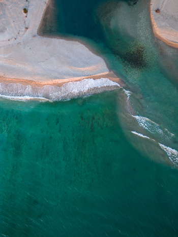Aerial view of a turquoise coastal estuary where a river meets the sea with gentle waves breaking on the sandy shore and clear water in Albania.