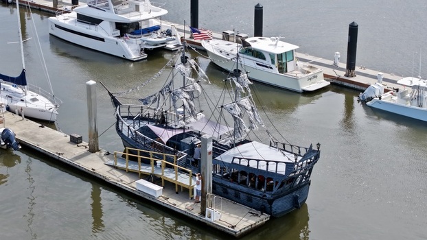 Aerial view of a dark tattered pirate ship replica docked alongside modern yachts in a serene marina Fernandina Beach Florida United States. Aerial view of a dark tattered pirate ship replica docked alongside modern yachts in a serene marina Fernandina Beach Florida United States.