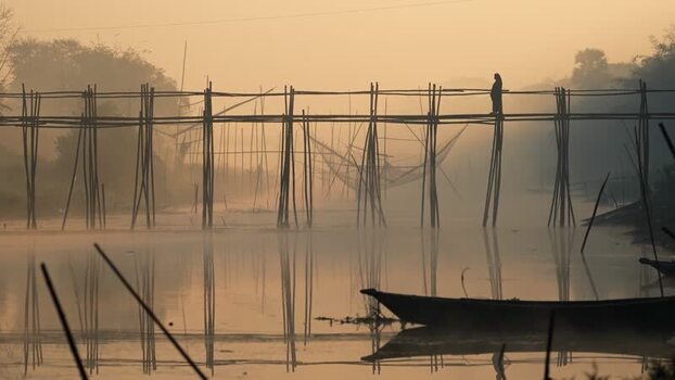 View of a person on a bamboo bridge over a misty river Bangladesh.