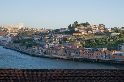View of terracotta rooftops cascade into the Douro River where colorful buildings line the waterfront under a soft golden light Porto Porto District Portugal. View of terracotta rooftops cascade into the Douro River where colorful buildings line the waterfront under a soft golden light Porto Porto District Portugal.