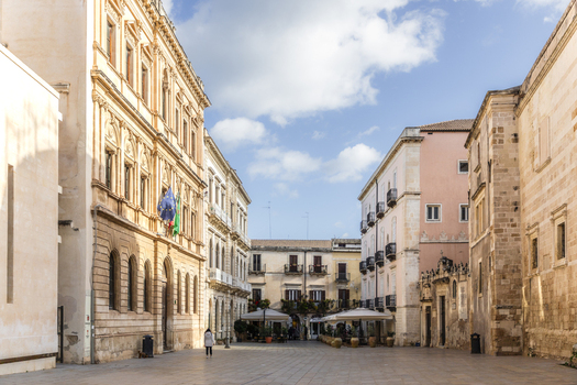 View of aged buildings basking in the sun s glow casting long shadows across the empty square a serene scene unfolds Ortigia Sicily Italy.