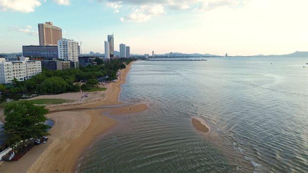 Aerial view of Jomtien Beach featuring high rise hotels lush green trees and calm sea water under a clear sky in Chon Buri Thailand.